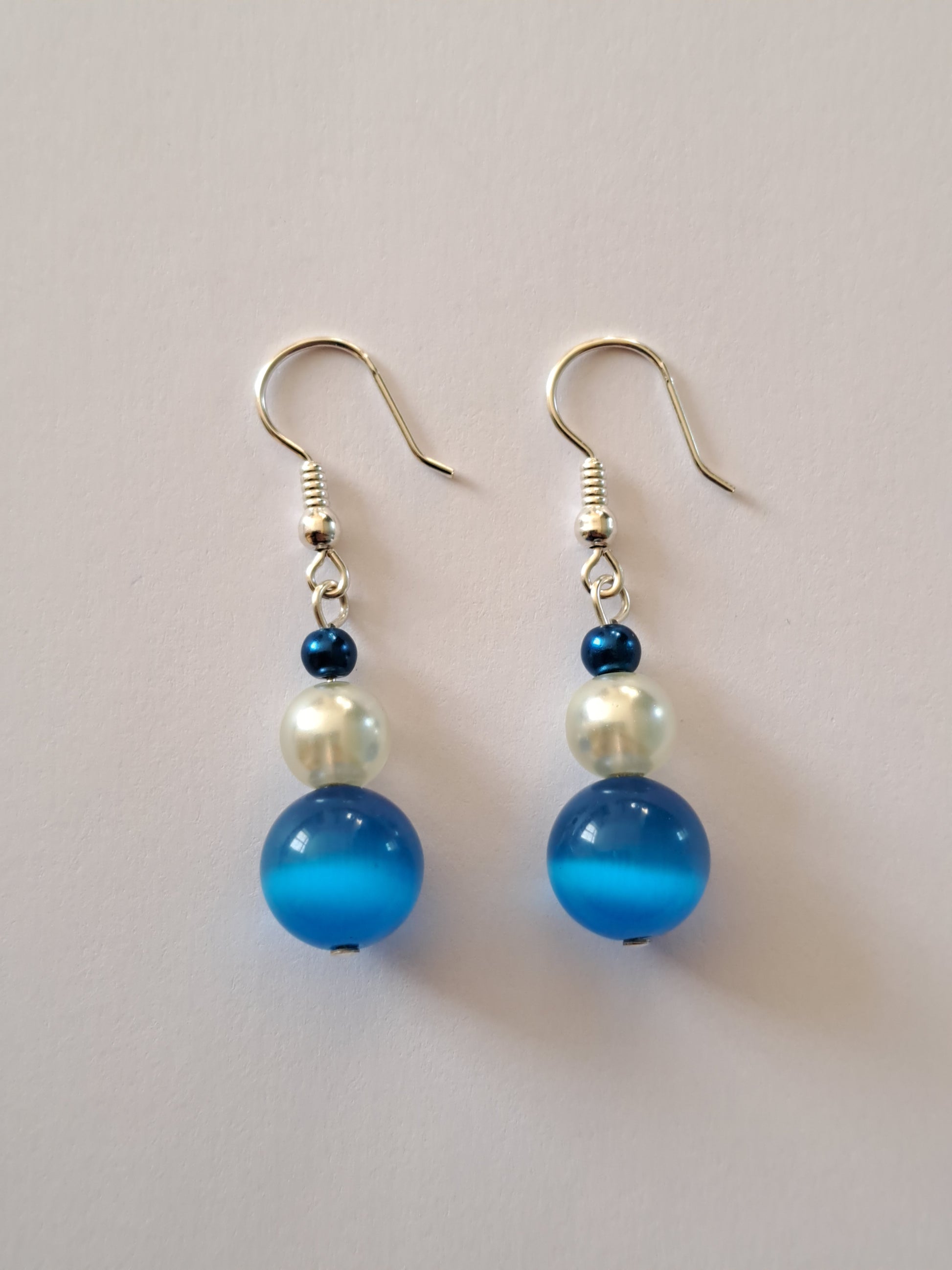 Boucles d'oreilles en argent avec perles nacrées blanches et oeil de chat bleue. Site de bijoux en ligne. France.
